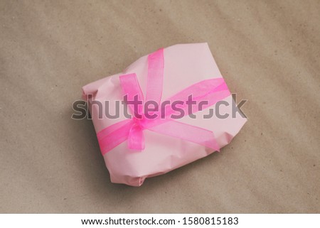 Soft pouch wrapped in craft paper and tie pink silk ribbon. Crumpled paper background texture. Delivery service. Online shopping.	
