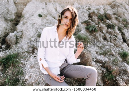 Gentle portrait of a beautiful girl or woman in a white blouse in the backlight on a sandy background