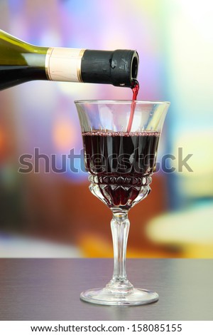 Red wine being poured into wine glass, on bright background