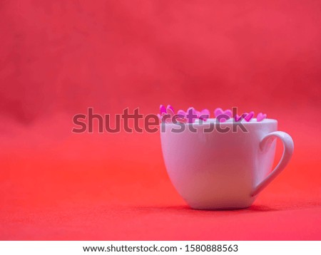 Closeup of white coffee cup and pink paper sticker on vivid or vibrant red background for love, valentine, romance, wedding, greeting card concept and idea.