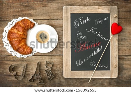 Cup of black coffee with croissant, blackboard and heart decoration on rustic wooden table. romantic french breakfast. Sentimental background with sample text Paris Amour Bonjour