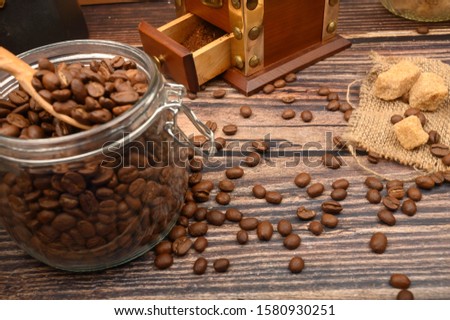 Wooden spoon in a glass jar with coffee beans, coffee grinder, pieces of brown sugar on a wooden background. Close up.