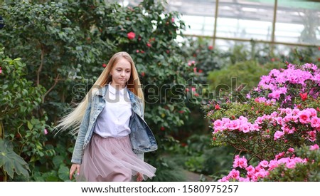 girl with long white hair in a denim jacket walks in a flowering garden