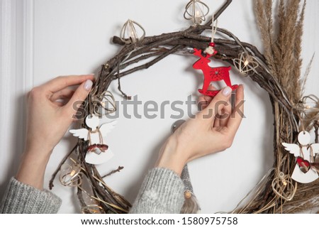 Woman makes a Christmas wreath.  Female hand's. Traditional  Сhristmas wreath on the front door inside.  Handmade wreathe with lights and toys.  Winter holiday's decoration.  
Lifestyle. 
