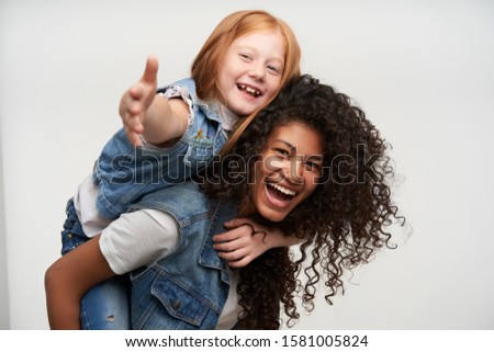 Portrait of overjoyed attractive ladies wearing family look while posing to camera over white background, being in high spirit and laughing cheerfully while having fun together