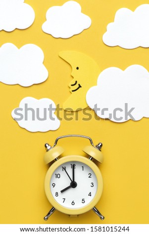 Yellow round alarm clock, moon and white clouds on the yellow background.