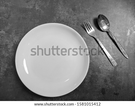 Empty White ceramic plate with fork and spoon on gray stone concrete table background. Copy space. Menu Recipe Concept
