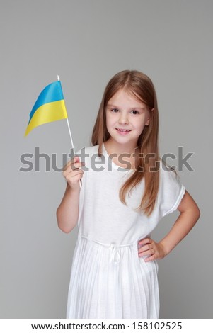 Portrait of a pretty young girl with a Ukrainian flag on a gray background on Holiday