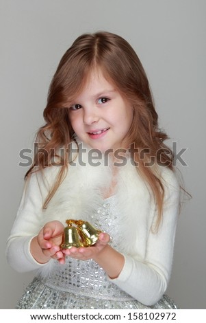 Beautiful cheerful little girl in a dress holding a shiny Christmas bells on a gray background/Christmas and New Year decoration
