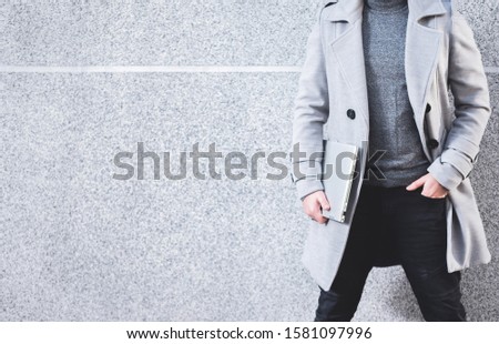 Cropped picture of handsome elegant businessman holding  laptop with copy space on grey texture background. Wallpaper, billboard picture. Concept of busy life