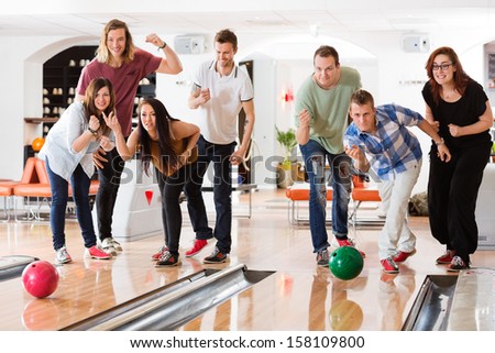 Young friends bowling while people cheering in club