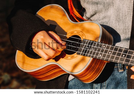 Red-haired girl with long hair plays on the ukulele in the park. School, music education concept, student learns to play the string instrument. Hands of a musician, classical, melody, creativity