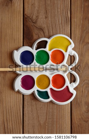 Set of colorful dry watercolor paints in a white plastic palette and brushes on a wooden table.