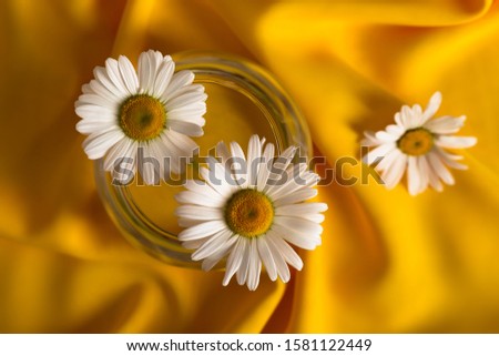 Chamomile flowers in a round glass vase on a yellow woven surface. View from above.