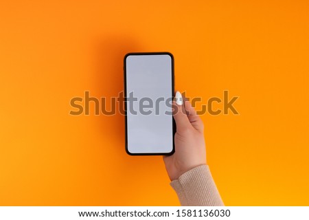 Female hand holding and touching on mobile smartphone with white screen. Isolated on Orange. Photo template for any images on mobile phone display Layout with easily removable phone monitor background