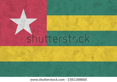 Togo flag depicted in bright paint colors on old relief plastering wall. Textured banner on rough background