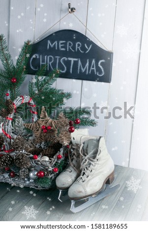 Merry Christmas background with wicker basket, skates for figure ice skating, fir tree on shabby wooden old table, blackboard with inscription on white wall, New Year holiday rustic home interior.