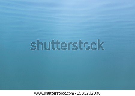 Picture of blue to green shades of water mass from under water. Fine structure of waves from below. Light blue to azure color transition.