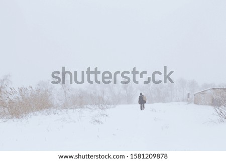 A rustic man is walking down the street in winter with a yellow backpack. Snow blizzard.