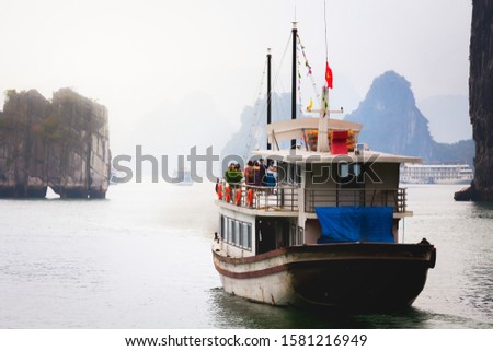 Landscape view with travelers enjoy sightseeing and take pictures on wooden cruise tour in Halong Bay. Nature seascape scene with tourist boats and old limestone islets in Ha long, Quang Ninh, Vietnam