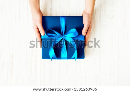 Male hands with blue box on white wooden background.