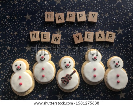 Gingerbread snowman cookies with ukulele,  and Happy New Year in 3d wooden alphabet letters on a blue background with glitter stars