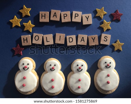 Gingerbread snowman cookies and Happy Holidays in 3d wooden alphabet letters on a blue background with stars