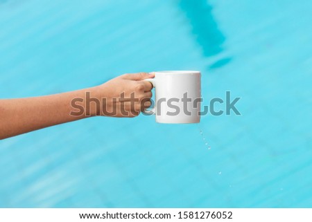Hand with white blank cup for mockup near a pool
