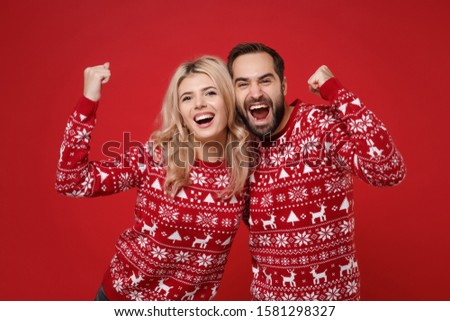 Funny young couple guy girl in Christmas knitted sweaters posing isolated on red background in studio. Happy New Year 2020 celebration holiday party concept. Mock up copy space. Doing winner gesture
