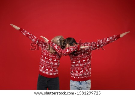 Young couple guy girl in Christmas sweaters posing isolated on bright red background studio portrait. Happy New Year 2020 celebration party concept. Mock up copy space. Showing DAB dance gesture