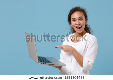 African american doctor woman isolated on blue background. Female doctor in white medical gown pointing finger on laptop pc computer. Healthcare personnel medicine health concept. Mock up copy space