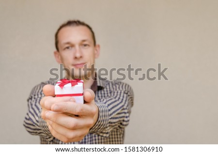 dark-haired man with a smile holds out a gift box isolated on a light background, copying the space. Holiday concept