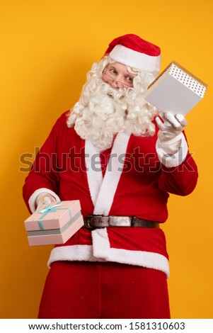 Santa Claus holds two gift boxes in his hands and poses on a yellow background