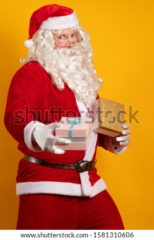 Santa Claus holds two gift boxes in his hands and poses on a yellow background