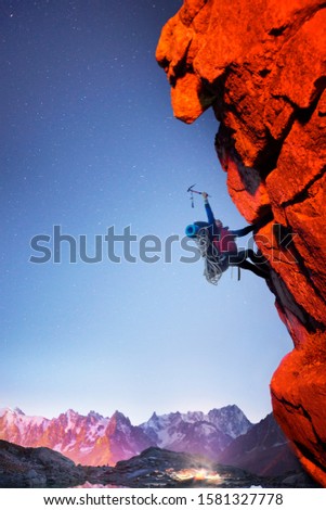 A symbolic picture with a climber on a sharp stone rock with a rope and an ice ax on a fantastic alpine mountain landscape with stars in the Himalayas