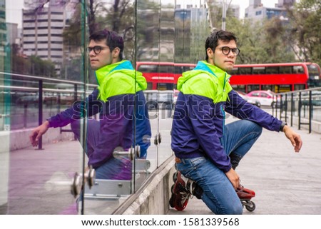Young street Skater sitting and leaning on a wall made of glass in the street