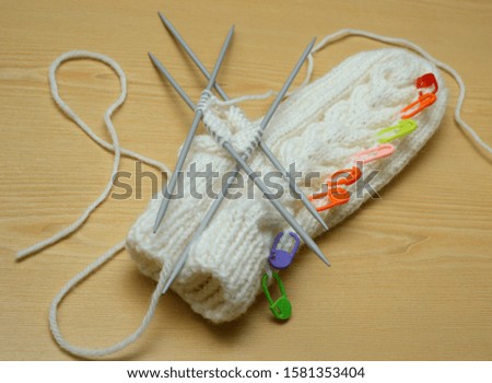white mitten and knitting needles on wooden background