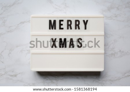 Simple Merry Christmas "Xmas" light board with christmas decorations on a white marble background. Green, red, and gold accents. 