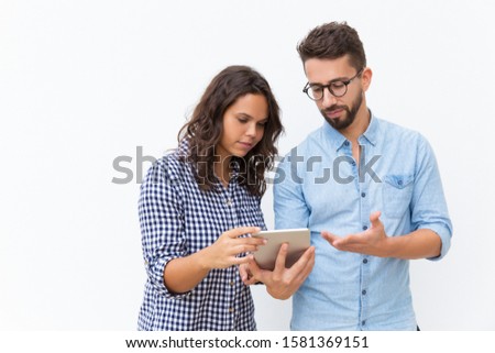 Serious puzzled couple reading message on tablet screen. Young woman in casual and man in glasses in glasses posing isolated over white background. Networking concept