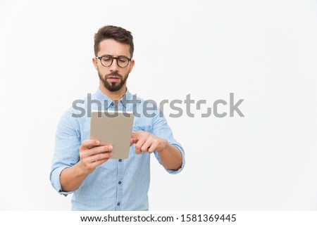 Focused professional working on tablet. Handsome young man in casual shirt and glasses standing isolated over white background. Digital communication concept