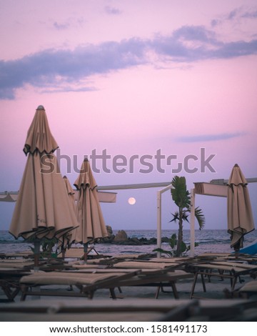 Empty beach resort at dusk with full moon under pink sky