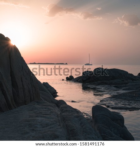 Rugged coastline at sunset with sun poking behind rock and creating rays