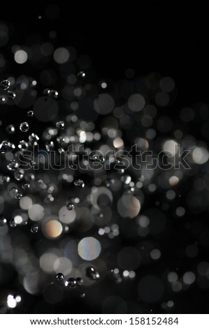Water drops fly in the air with defocused lights on dark background