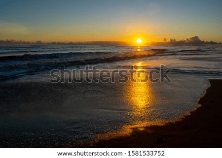 A sunset reflection from the horizon, across the ocean and waves on the shore in this view from a Kauai beach. 