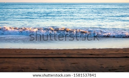Light reflects on the ocean, froth on the top of white waves is touched by a sunset glow, white waves contrast with dark sand.