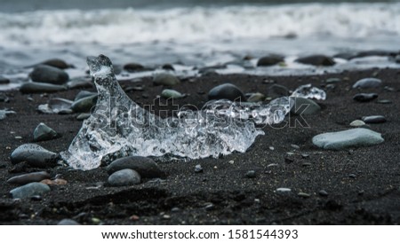 A block of ice lying on black sand in cloudy weather. Shot on the Diamond Beach in Iceland, a coastal area, where blocks of ice coming from a glacier lagoon are deposited by the tide.