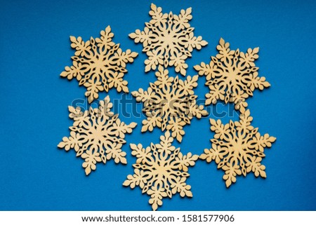 Seven delicate light brown wooden snowflakes on vivid classic blue textured cardboard background, displayed as a flower, top view with some space for text around, flat lay with laser cut wooden object
