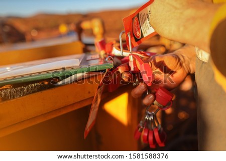 Close up miner hand placing personal red danger lock which is attached together with danger tag into isolation safety control permit lock box at the opening field prior to starting each work  Royalty-Free Stock Photo #1581588376