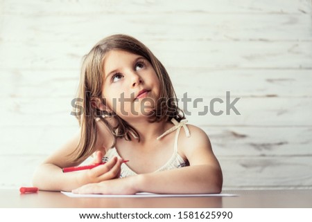 Portrait of beautiful thoughtful little girl with pencil in hand daydreaming and creating picture ideas in her mind. Creative process. Education and school concept