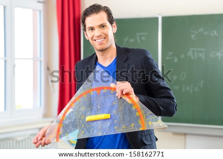 Teacher or docent in school holding a geometry triangle in front of a blackboard in school class 